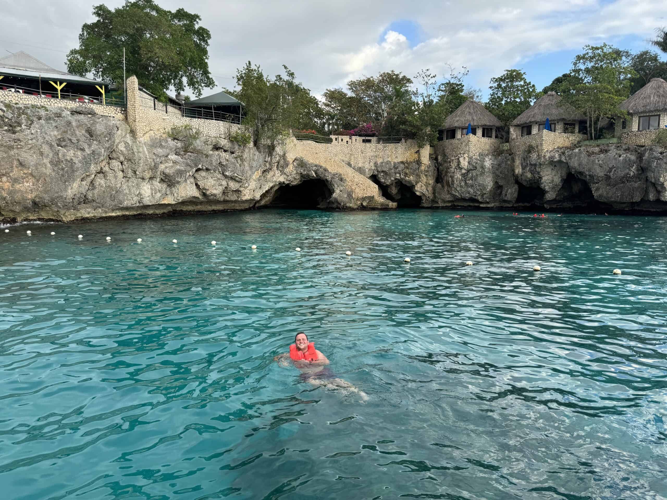 a young man swims near a cliff in an orange vest