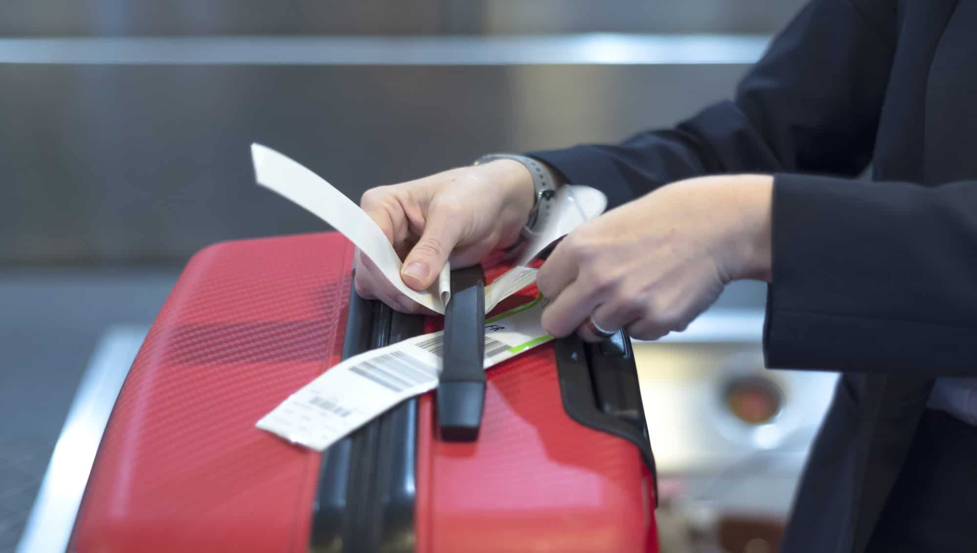 The Genius Trick to Keep Your Luggage From Getting Lost at the Resort 4 Heck-in employee attaches a luggage tag to suitcase